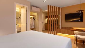 A hotel room with a bed, a seating area with a table and chairs, a shower area with a towel rack, and a mounted television.