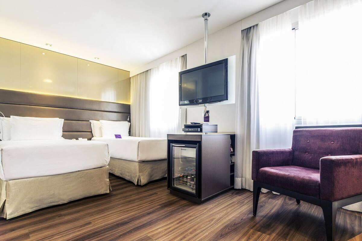 A hotel room with two beds, a TV, a small fridge, and a seating area.