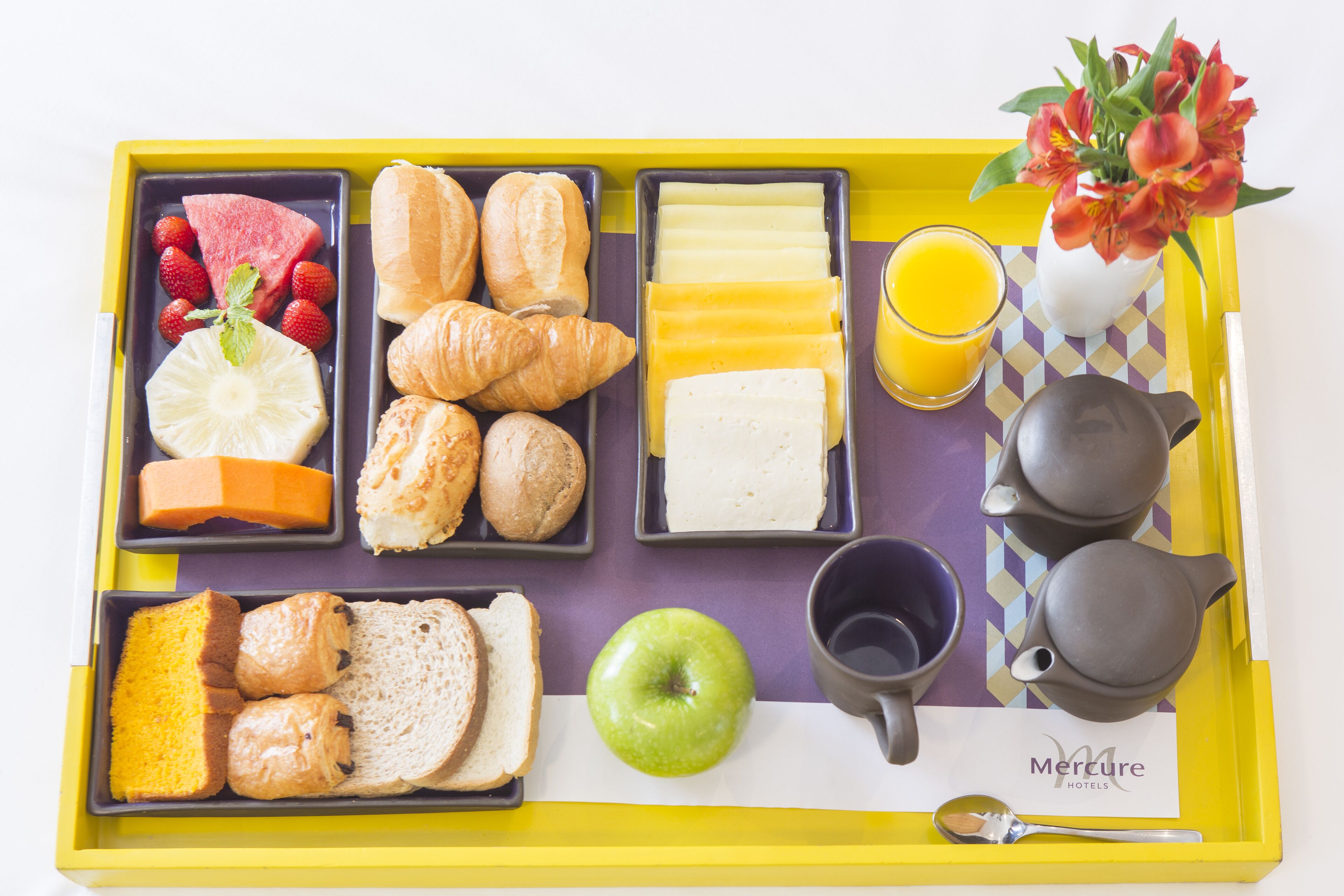 Un plateau de petit-déjeuner avec des croissants, des viennoiseries, du fromage, des fraises, de la pastèque, une pomme, du jus de fruits et une théière.
