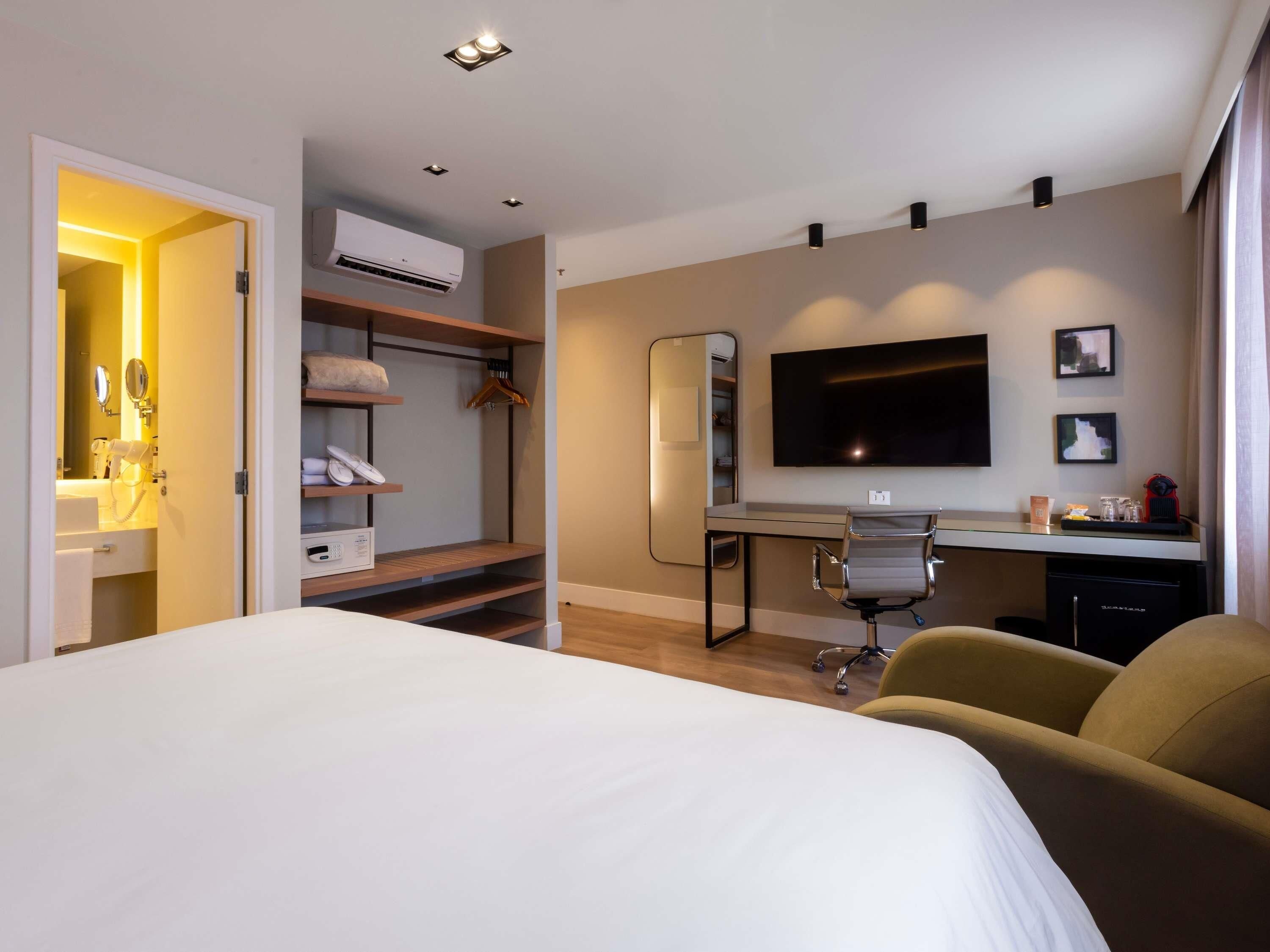 A hotel room with a bed, a desk with a chair, a TV, and a wardrobe.