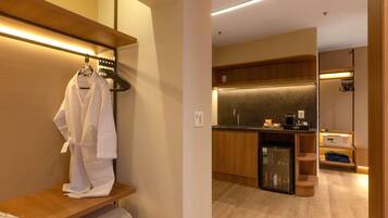 A modern hotel room with a wooden vanity, a robe hanging on a rack, and a kitchenette area.
