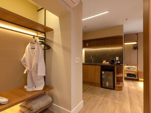 Habitació d'hotel moderna amb un tocador de fusta, una bata penjada en un suport i una zona de cuina equipada.
