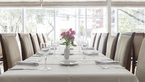 Una mesa de comedor preparada para una comida, con sillas, un florero con flores y vistas al exterior.