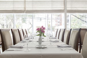 Uma mesa de jantar posta para refeição, com cadeiras, um vaso de flores e vista para o exterior.