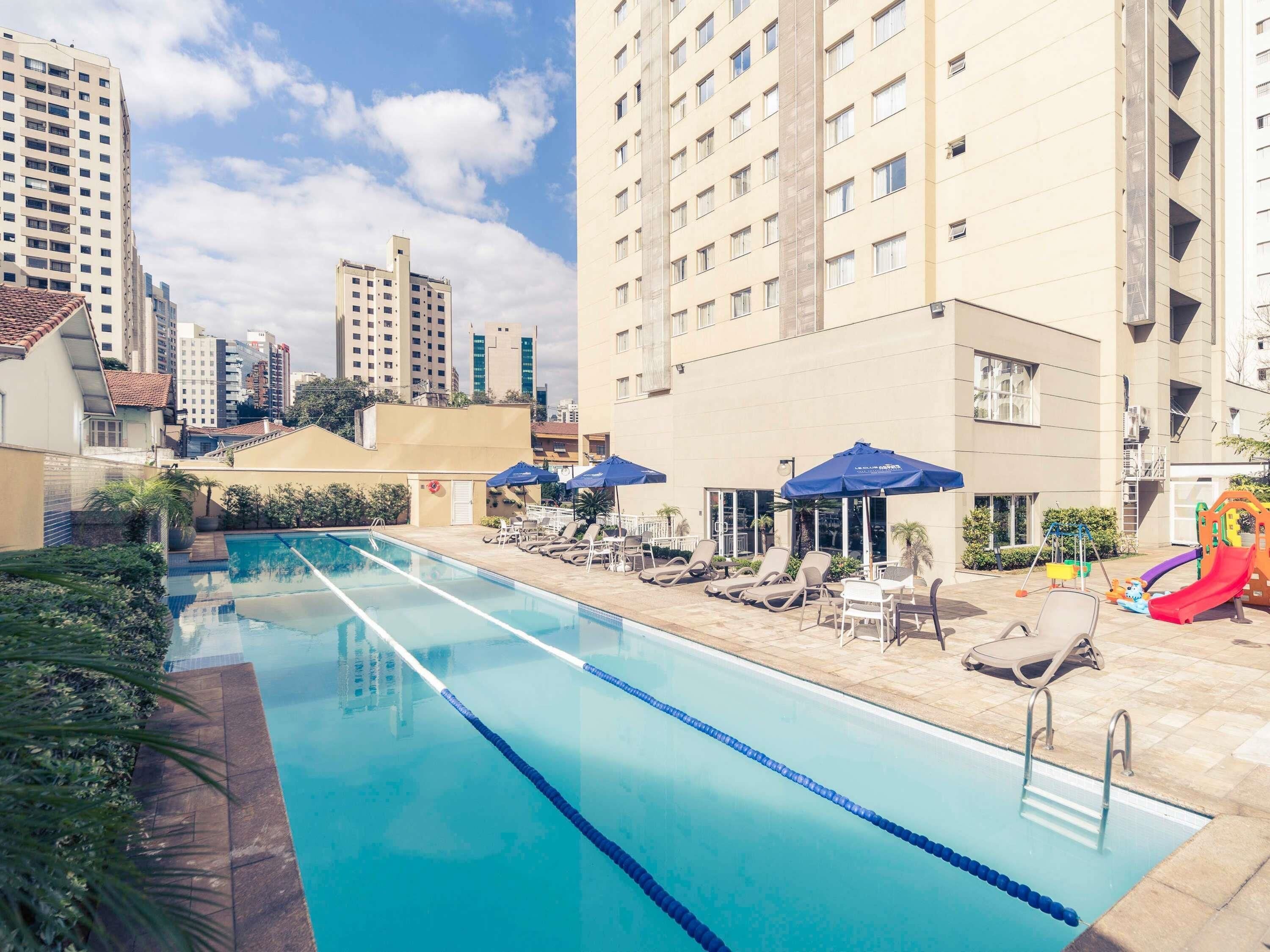 Une piscine entourée d’immeubles de grande hauteur, avec des chaises longues et des parasols.
