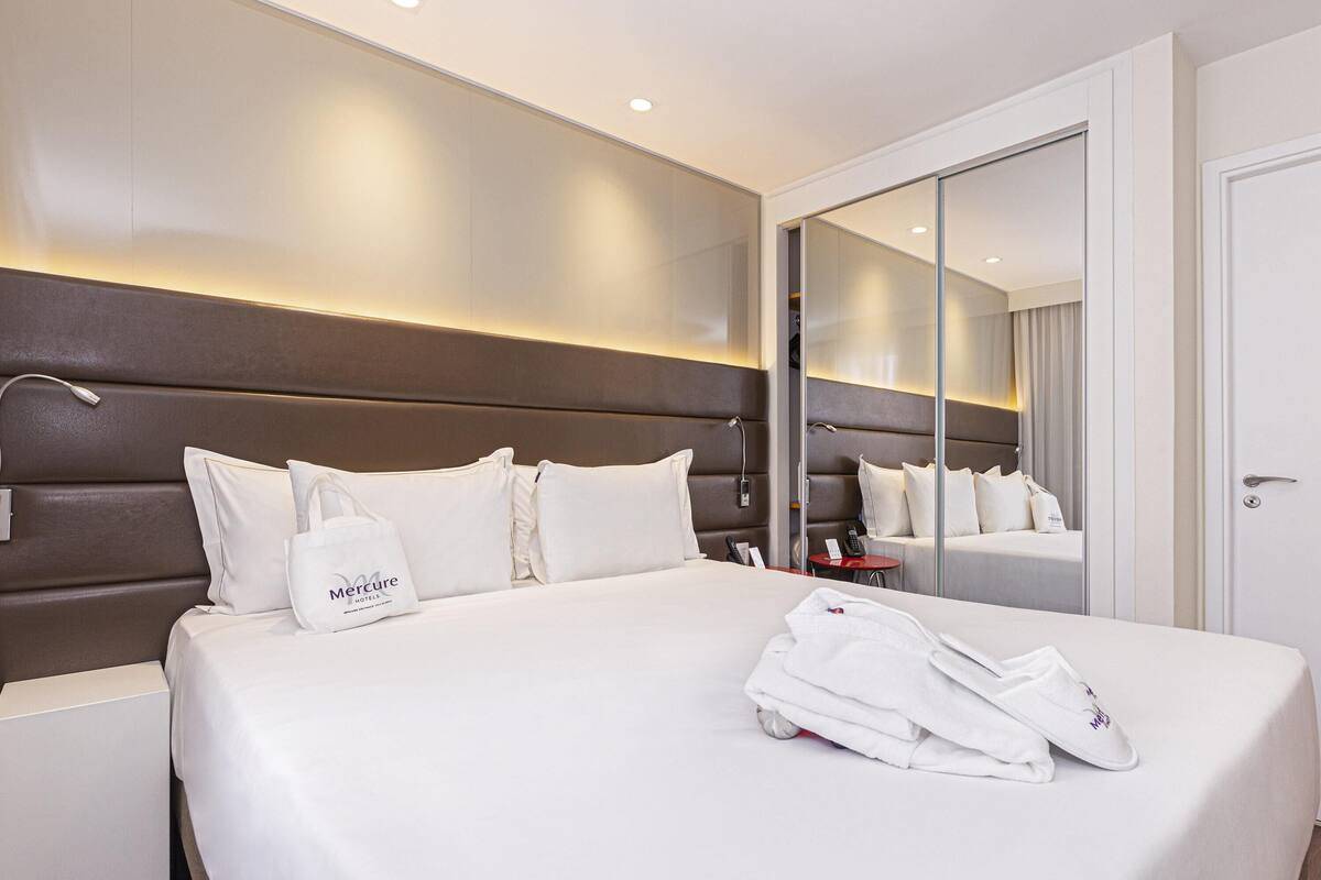 A hotel room with a large bed, a bedside table, a mirror, and a wardrobe.