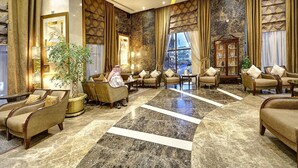 A spacious lobby with a marble floor, comfortable seating, and large windows offering a view of a cityscape.