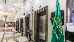 A hotel lobby with marble flooring, elevators, and a green flag with gold script.