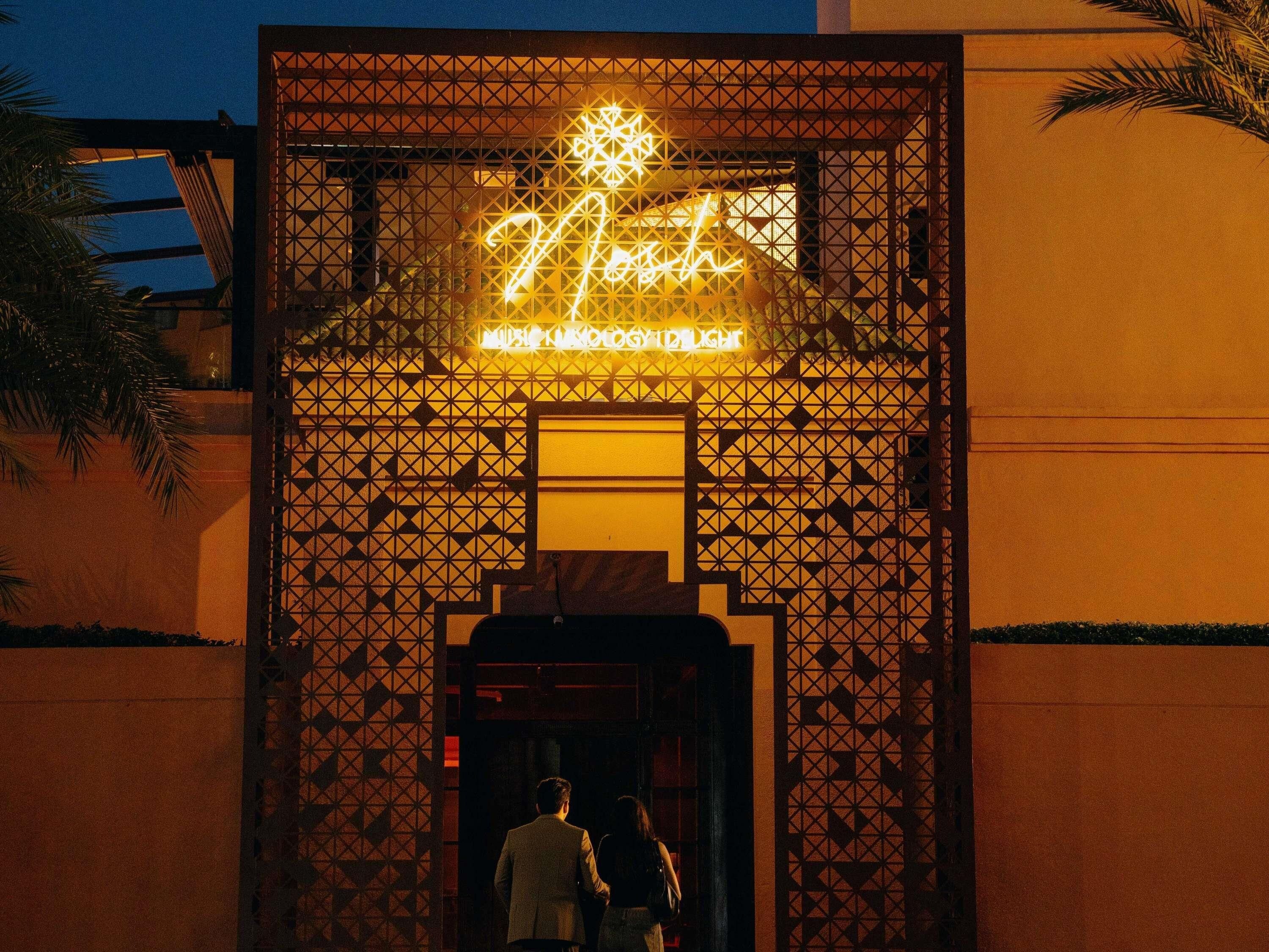 Entrada d'un edifici amb façana de disseny geomètric i un cartell de neó a la porta.