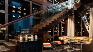 Un interior moderno con una escalera de cristal, una zona de estar con otomanas y una exhibición de conchas.