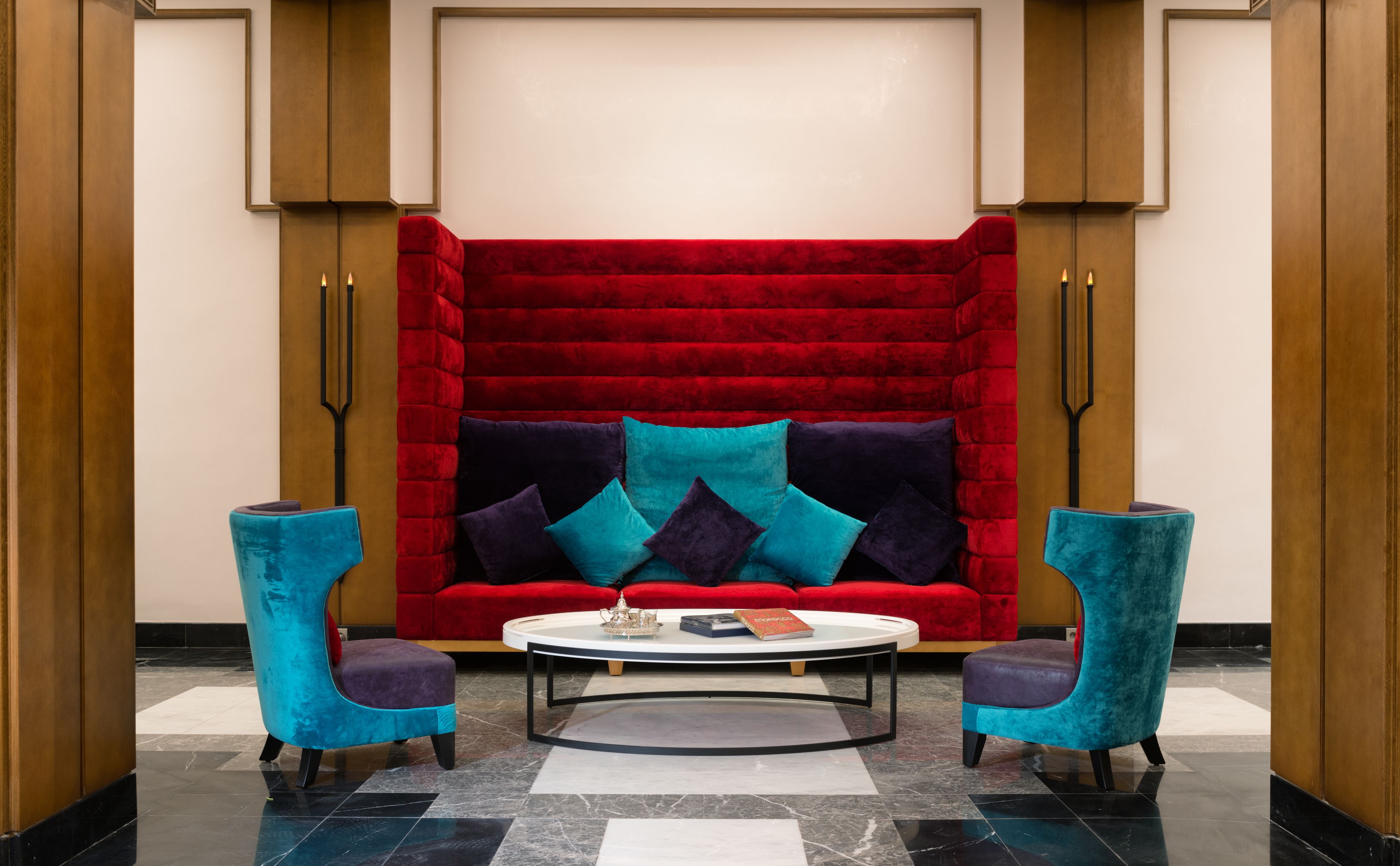 A modern lobby with a red velvet sofa, two turquoise armchairs, and a white coffee table.