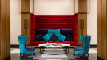 Eine moderne Lobby mit einem roten Samtsofa, zwei türkisfarbenen Sesseln und einem weißen Couchtisch.
