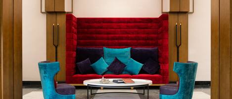 A modern lobby with a red velvet sofa, two turquoise armchairs, and a white coffee table.
