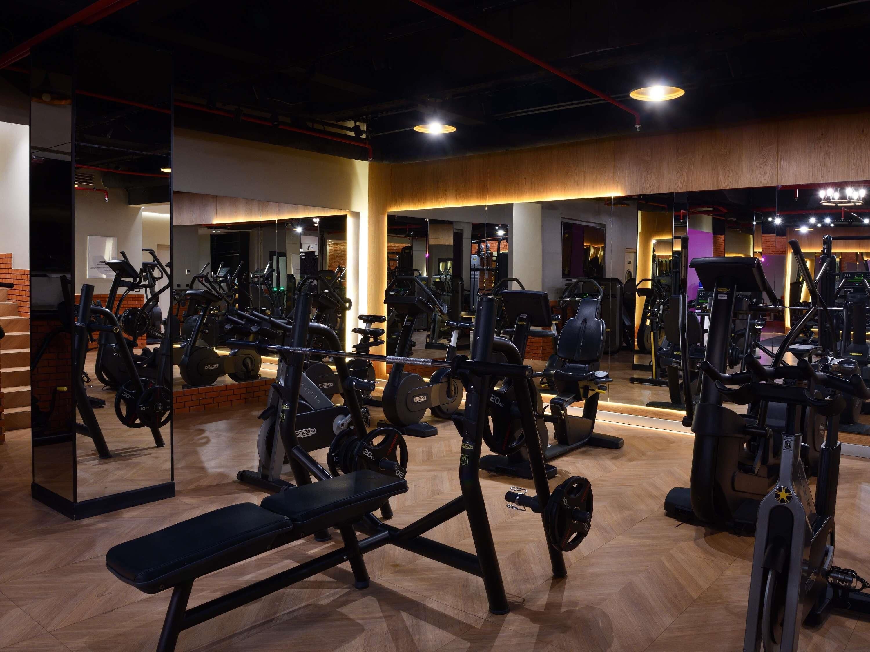 Une salle de sport équipée de divers appareils d’exercice, dotée d’un plancher en bois et d’un mur recouvert de miroirs.