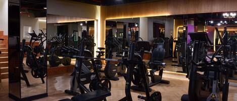 A gym with various exercise equipment, wooden flooring, and a mirrored wall.