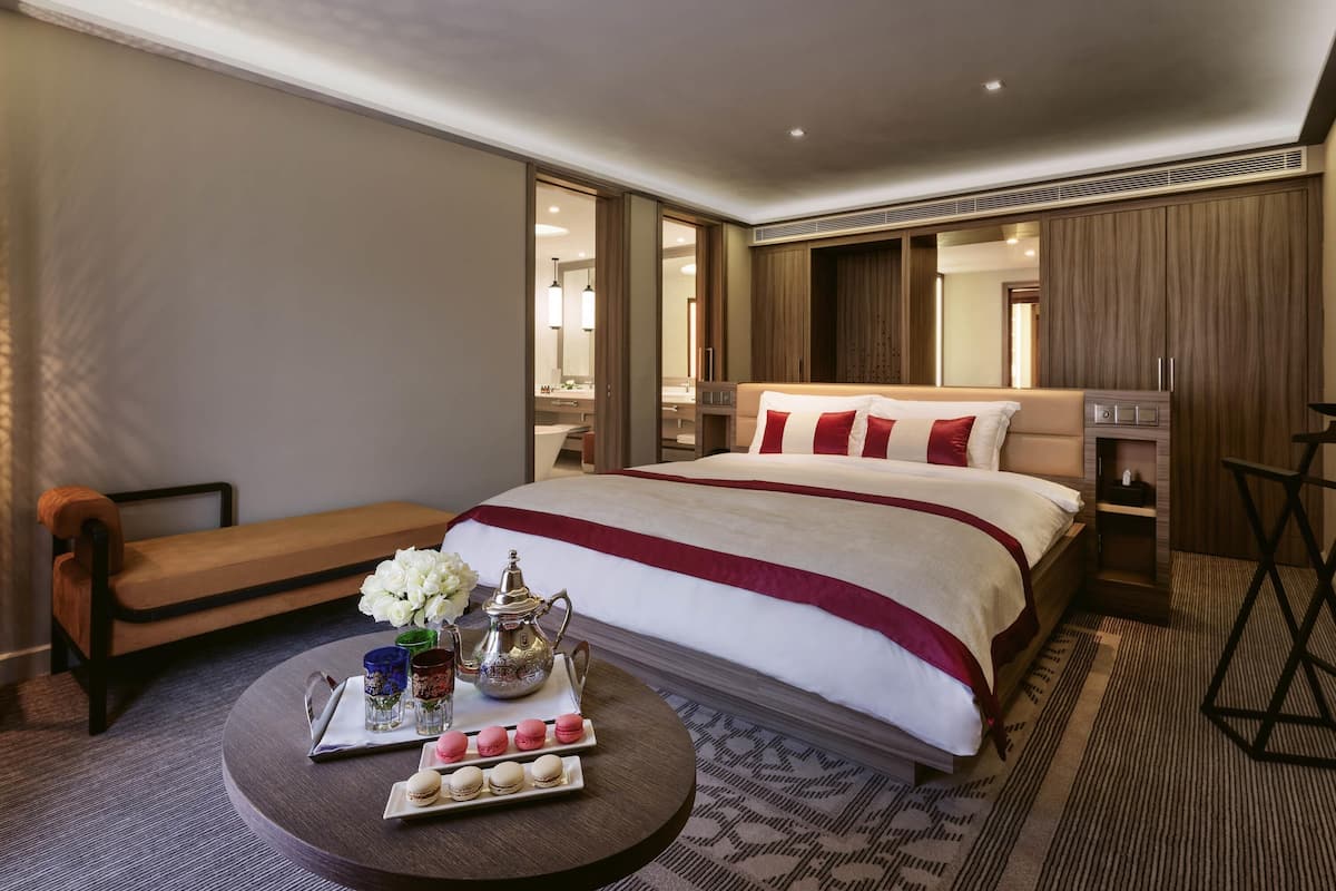Ein Hotelzimmer mit einem großen Bett, einem Nachttisch, einem kleinen runden Tisch mit Snacks, einem Spiegel und einem Kleiderschrank.
