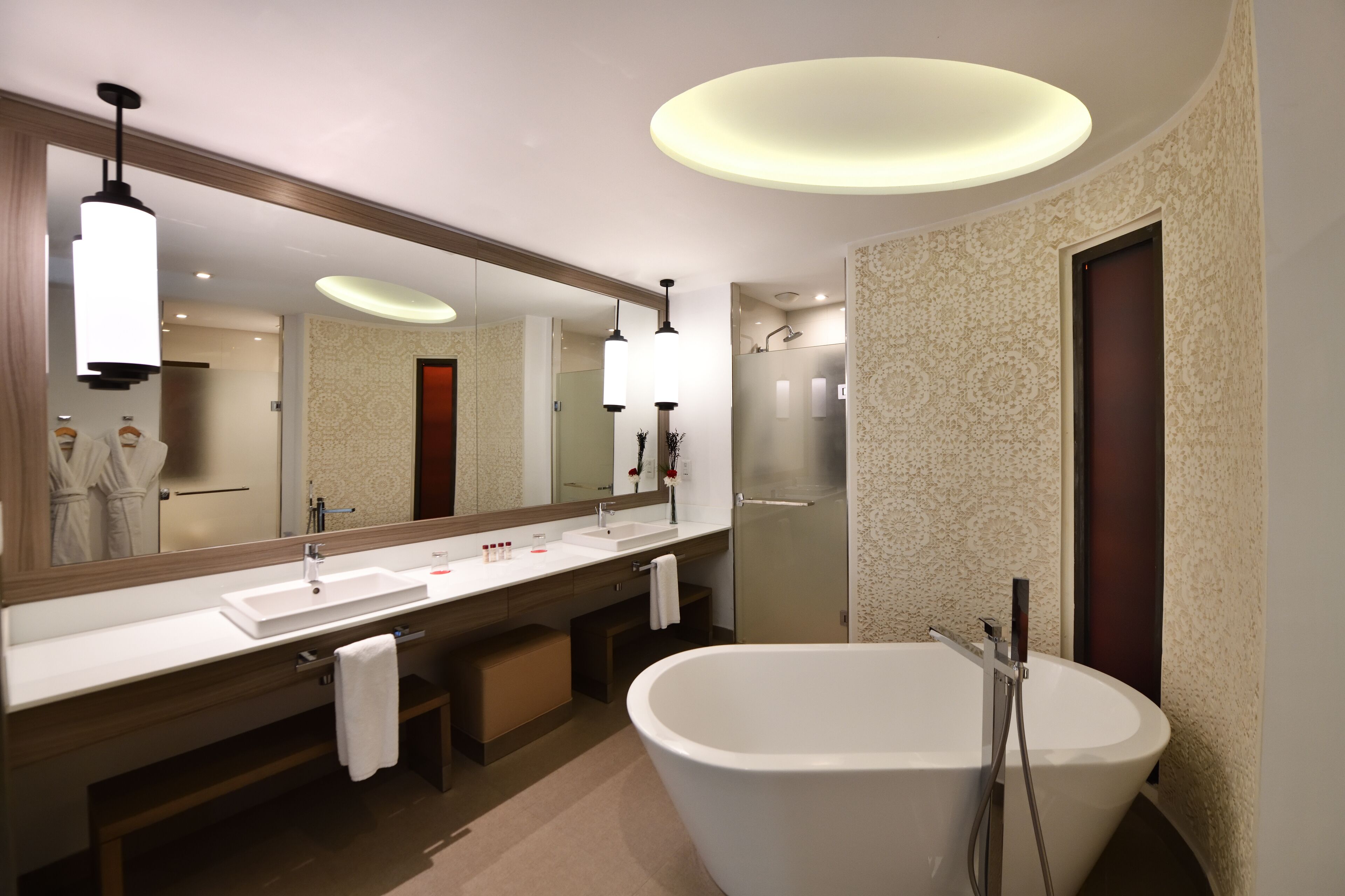 A modern bathroom with a large mirror, a white bathtub, and a vanity with a sink and towel rack.