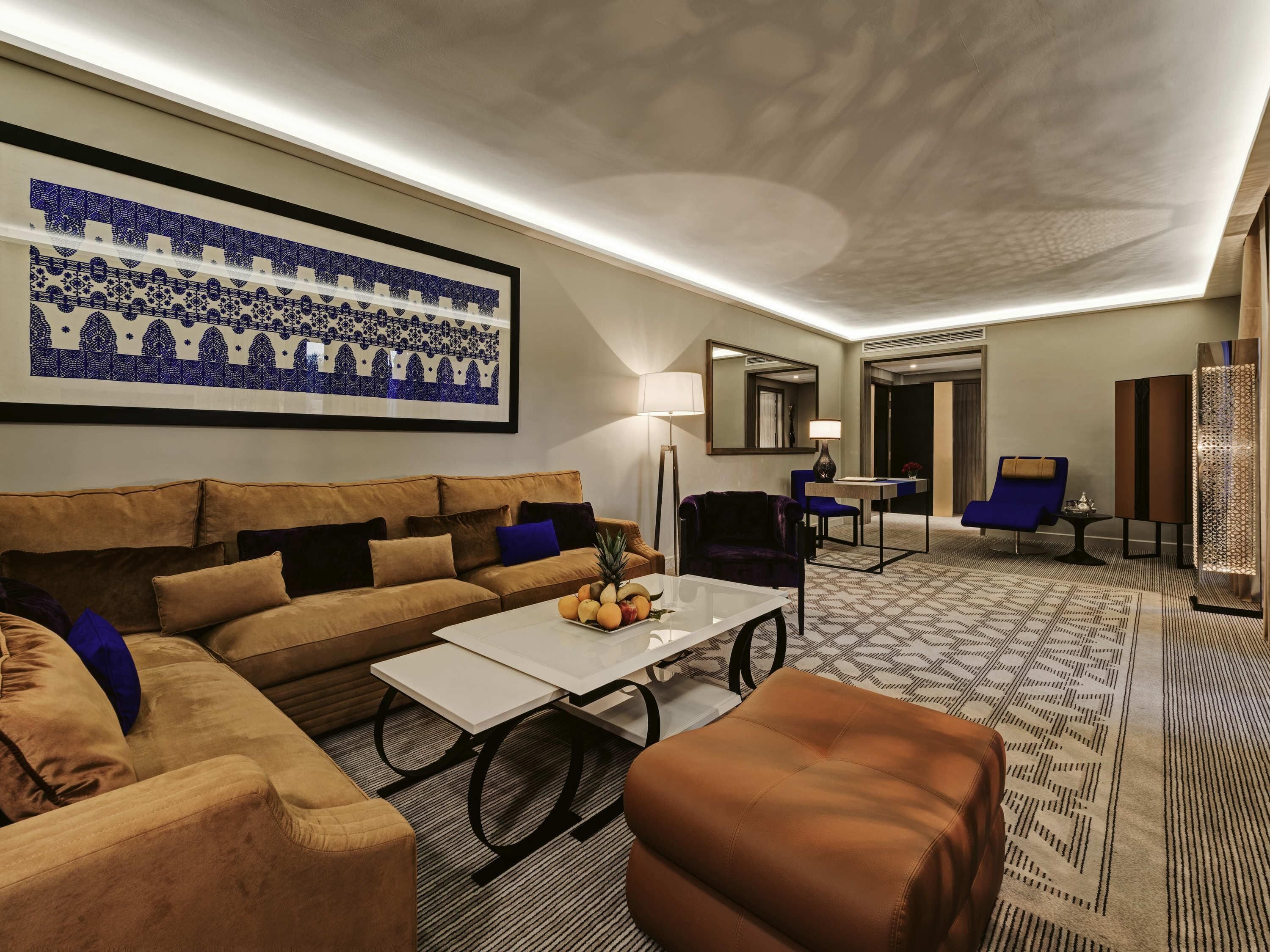A hotel room with a sofa, armchair, coffee table, and a decorative wall piece.