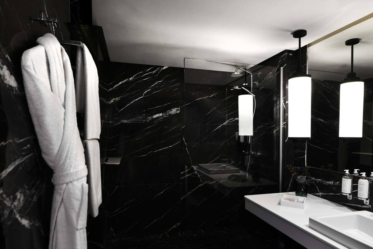 Ein modernes Badezimmer mit Marmorwand, Waschbecken in Weiß und einem Bademantel an einem Haken.