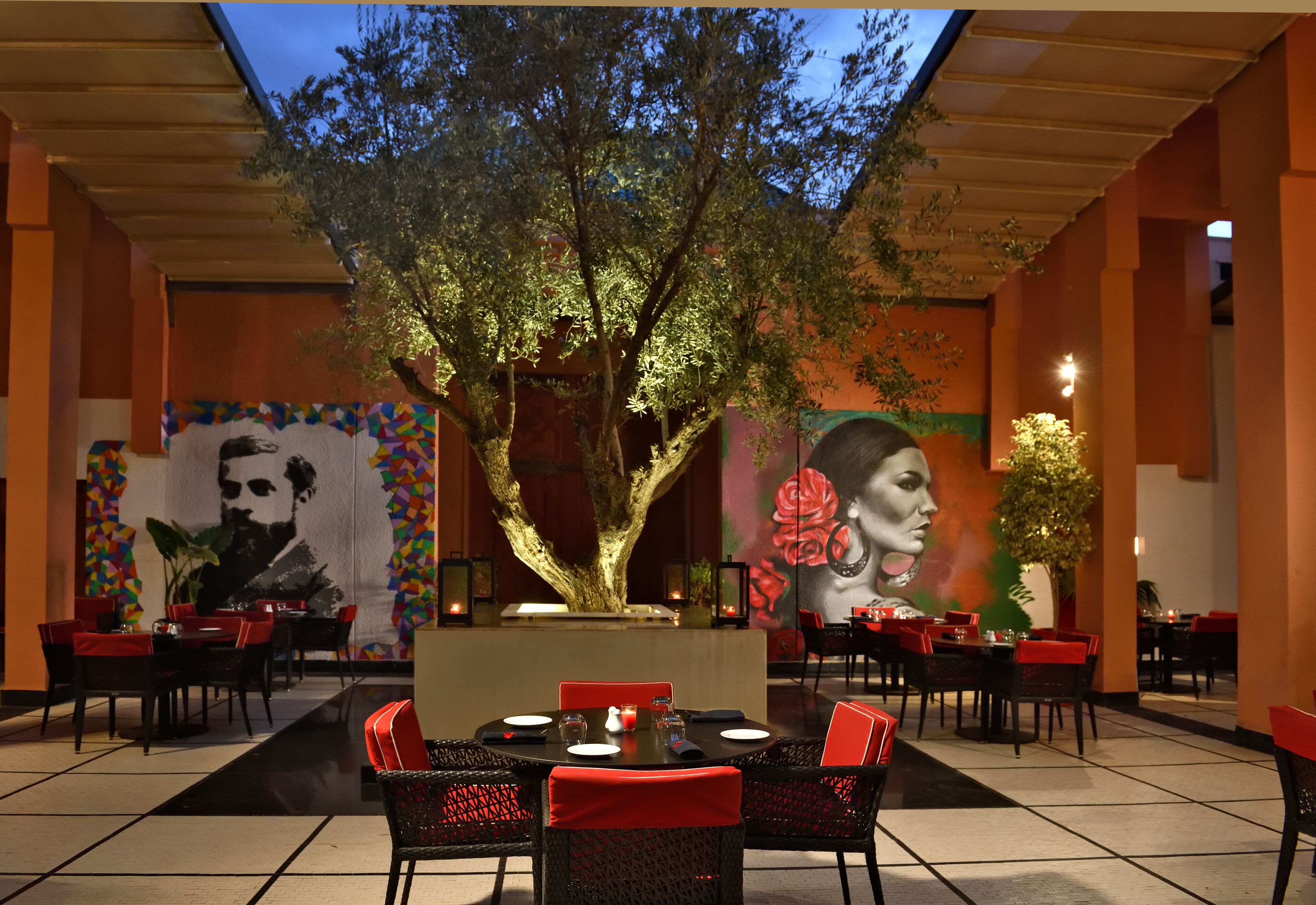 Un restaurante con sillas rojas, una mesa central y un gran árbol en el centro.