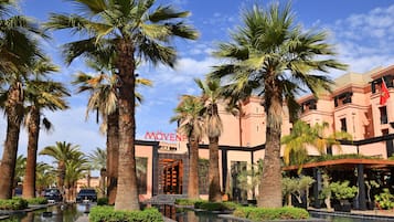 A hotel with palm trees, a pool, and a building with a sign that reads "Moven".