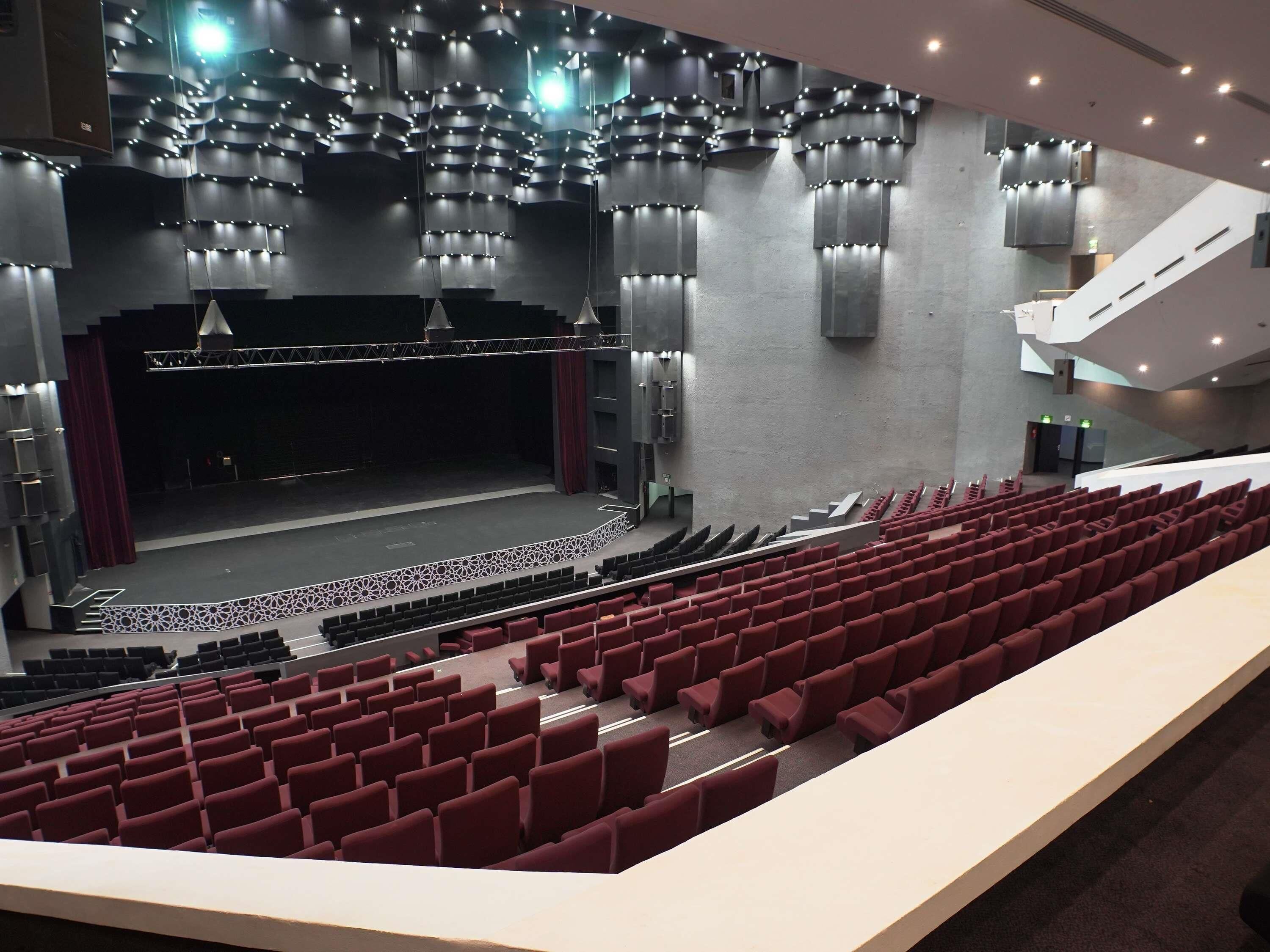 A modern theater with a stage, red seating, and contemporary lighting fixtures.