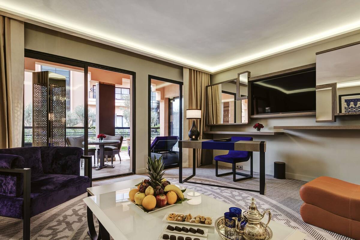 Ein modernes Hotelzimmer mit einer Sitzecke, einem Essbereich, einem Fernseher und einem Balkon mit Gartenmöbeln.