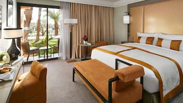 A hotel room with a large bed, a desk with a lamp, a chair, and a view of the outdoors.
