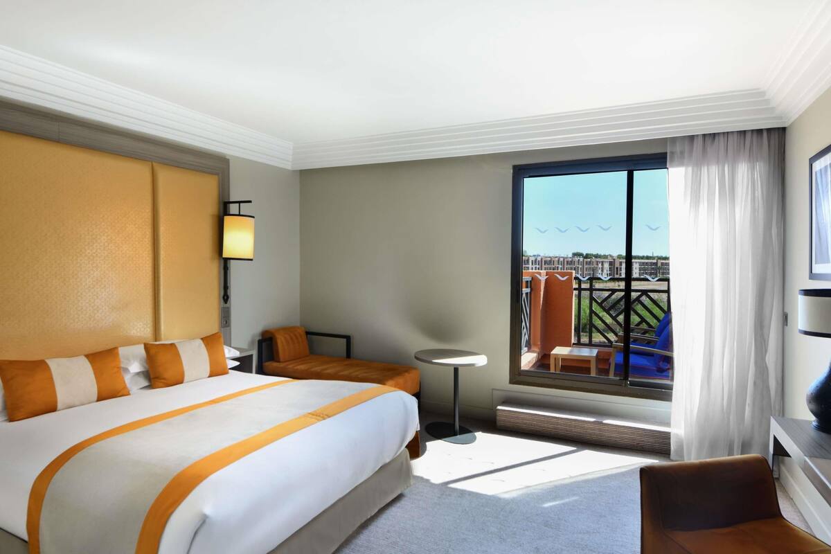 Ein Hotelzimmer mit einem großen Bett, einem Schreibtisch, einem Stuhl, einem kleinen Tisch und einem Balkon mit Blick.