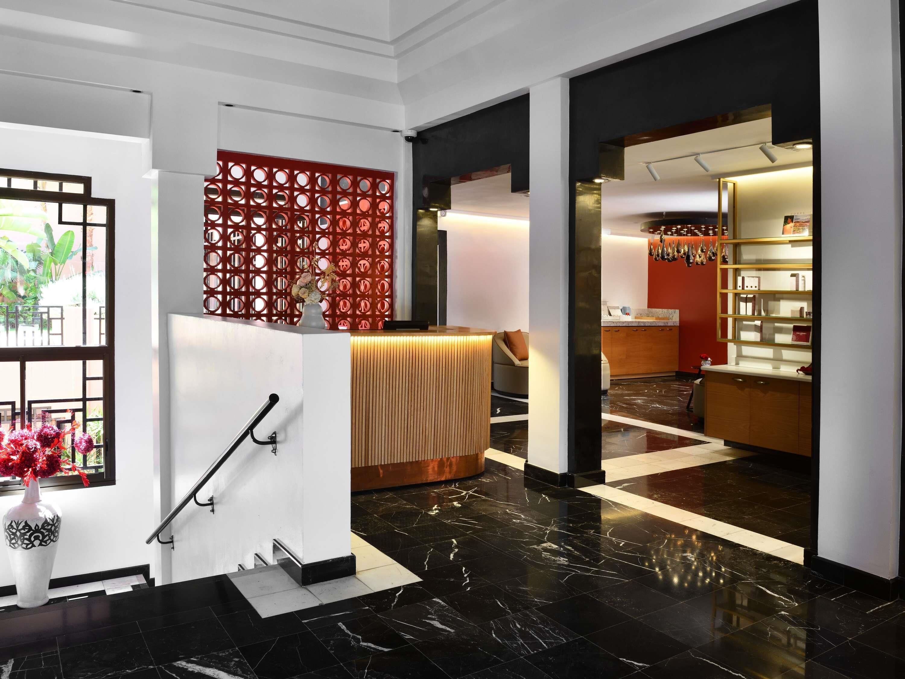 A modern hotel lobby with a reception desk, a staircase, and a kitchen area visible through an open door.