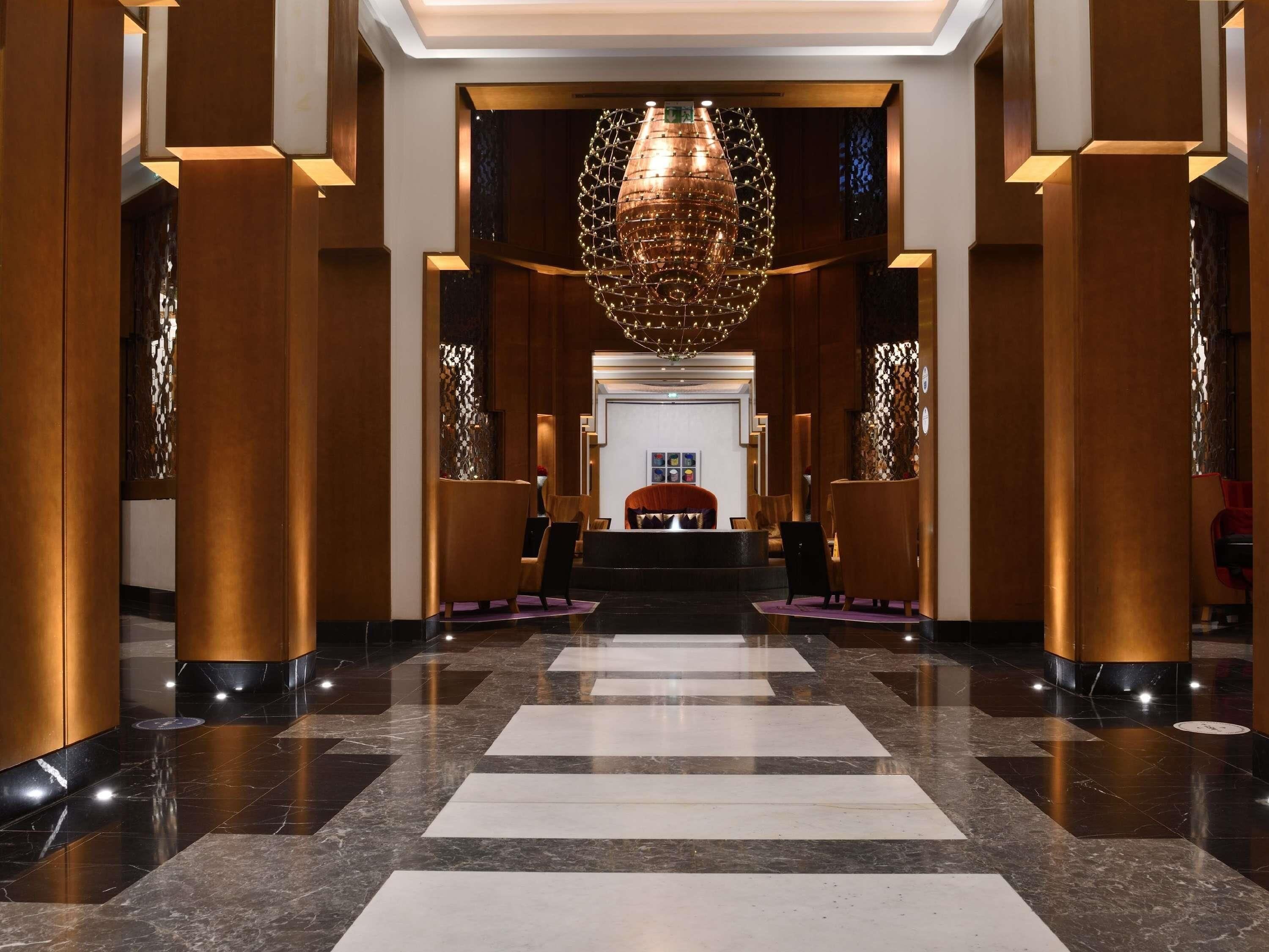 Un vestíbulo de hotel con un mostrador de recepción central, una araña y un mostrador de registro.