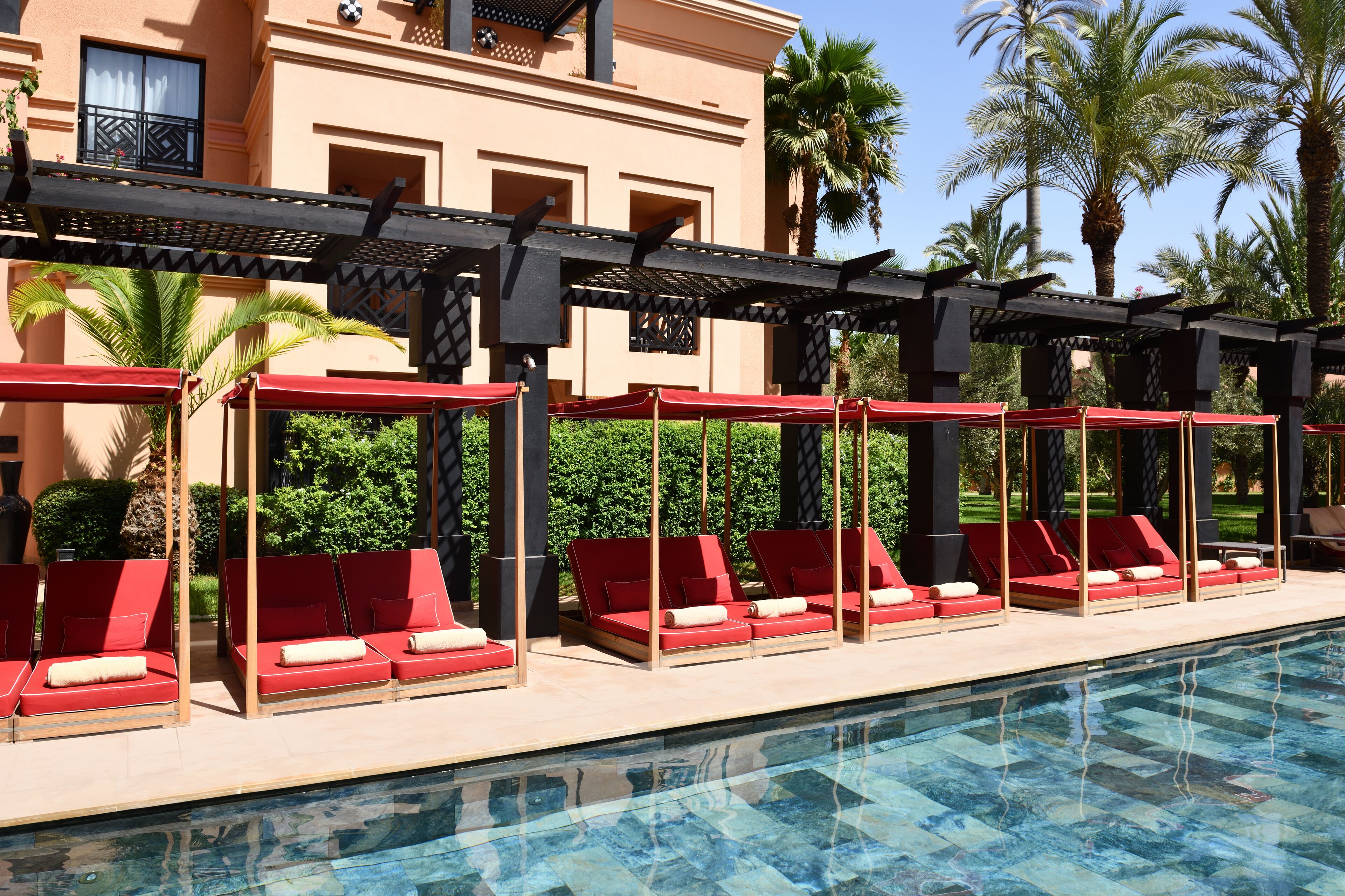Zona de piscina con sillones rojas y una estructura de pérgola.