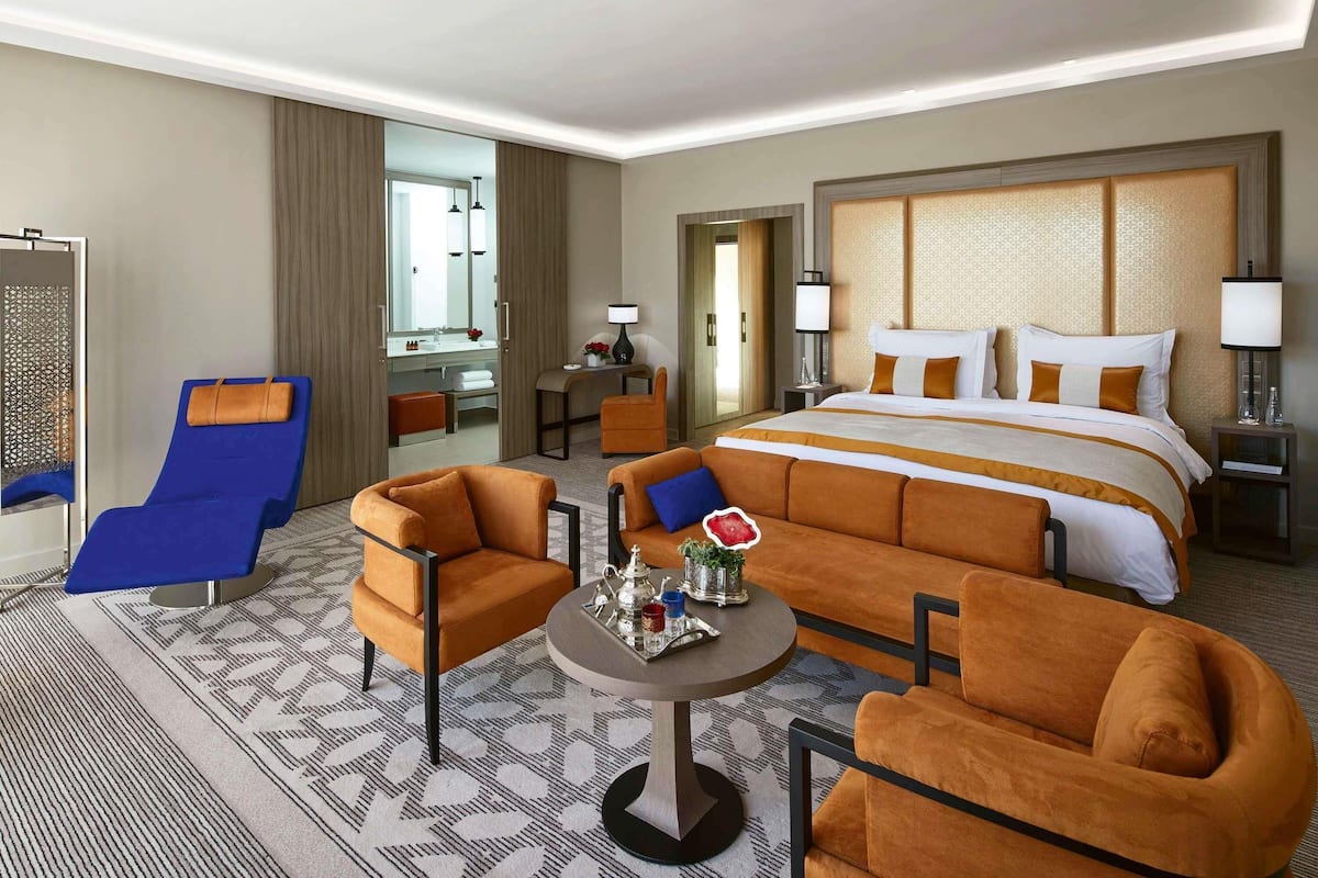 Ein Hotelzimmer mit einem großen Bett, zwei Sesseln, einer Couch, einem kleinen Tisch und einem durch eine offene Tür einsehbarer Badezimmer.