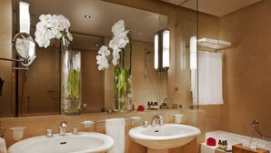 A bathroom with two sinks, a large mirror, and orchid flowers in glass vases. - Le Diwan Hotel Rabat - MGallery Collection (Rabat)