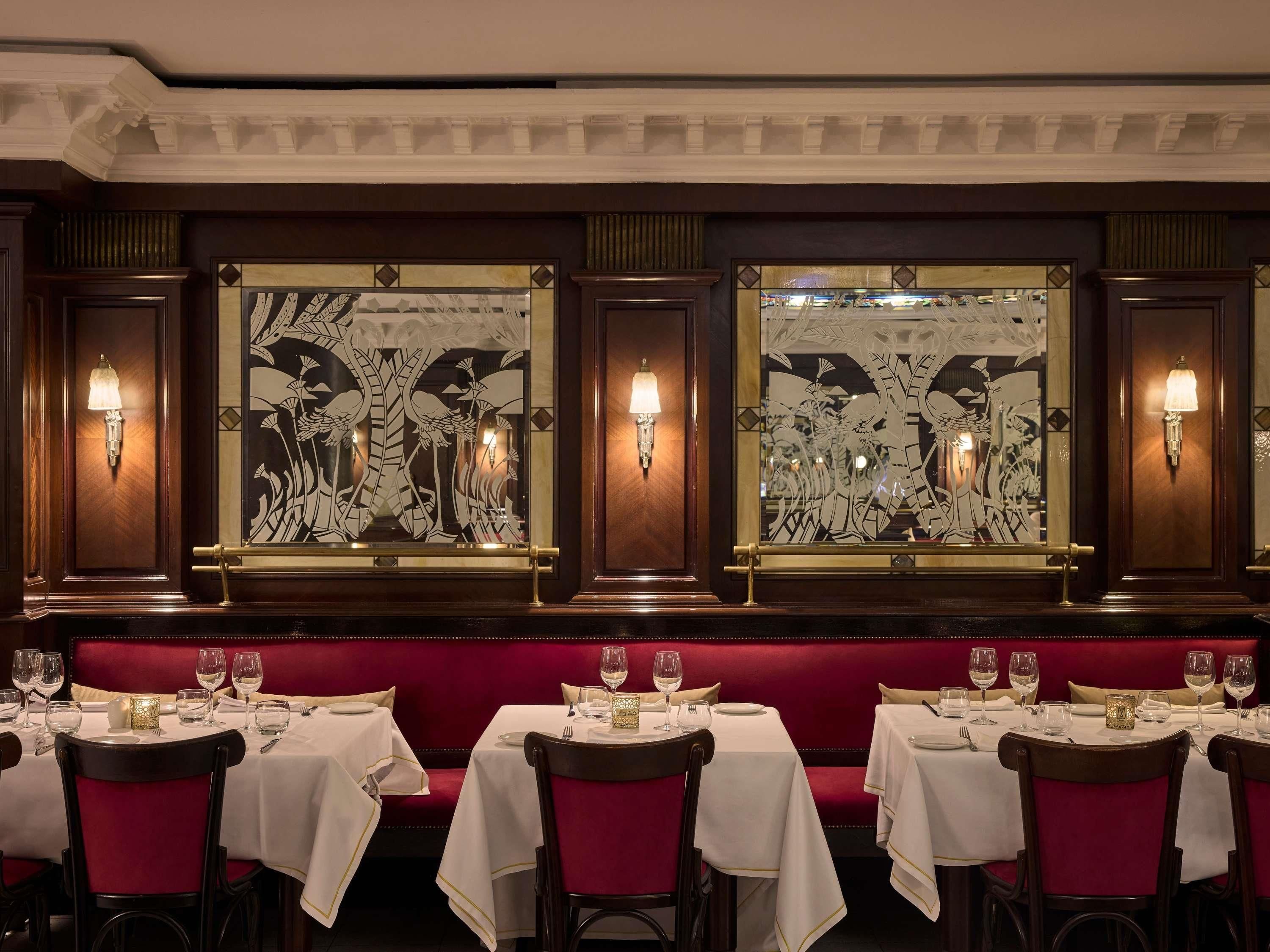 A restaurant with red upholstered booths, white tablecloths, and wall sconces.