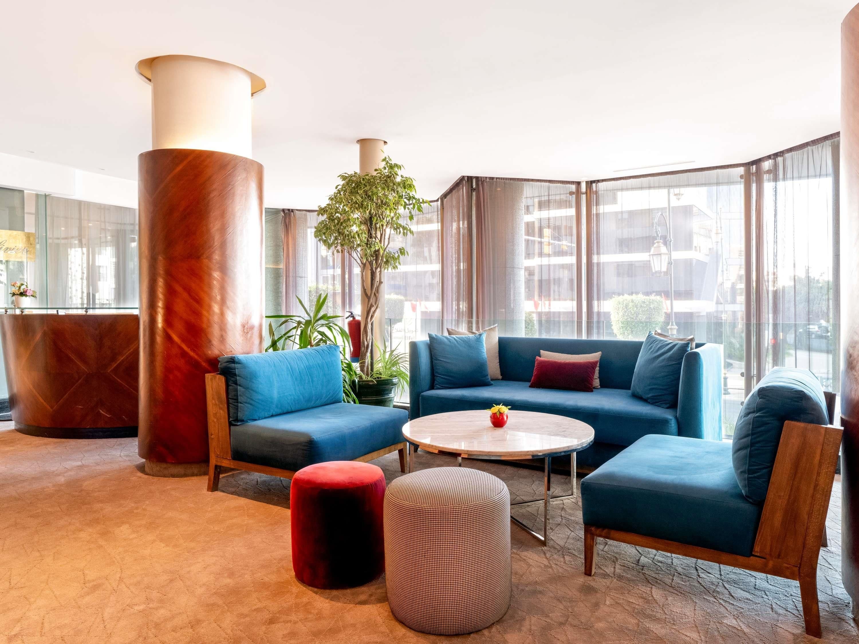 A modern lounge area with a blue sofa set, a round coffee table, and a red ottoman.