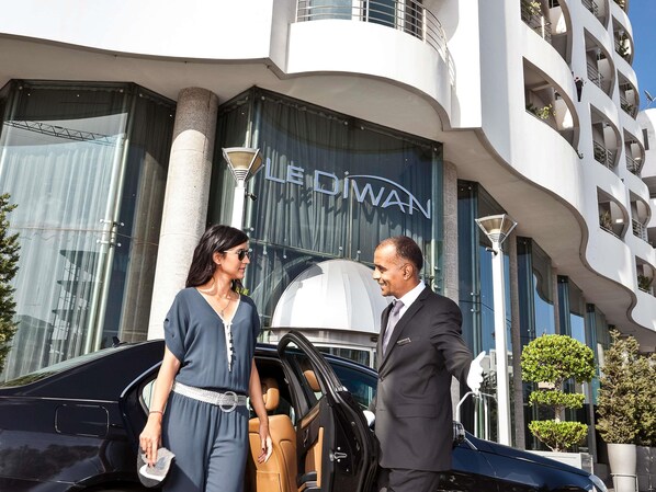 A man and a woman exiting a black car in front of a building with a modern design and the name "LE DIWAN" visible. - Le Diwan Hotel Rabat - MGallery Collection (Rabat)
