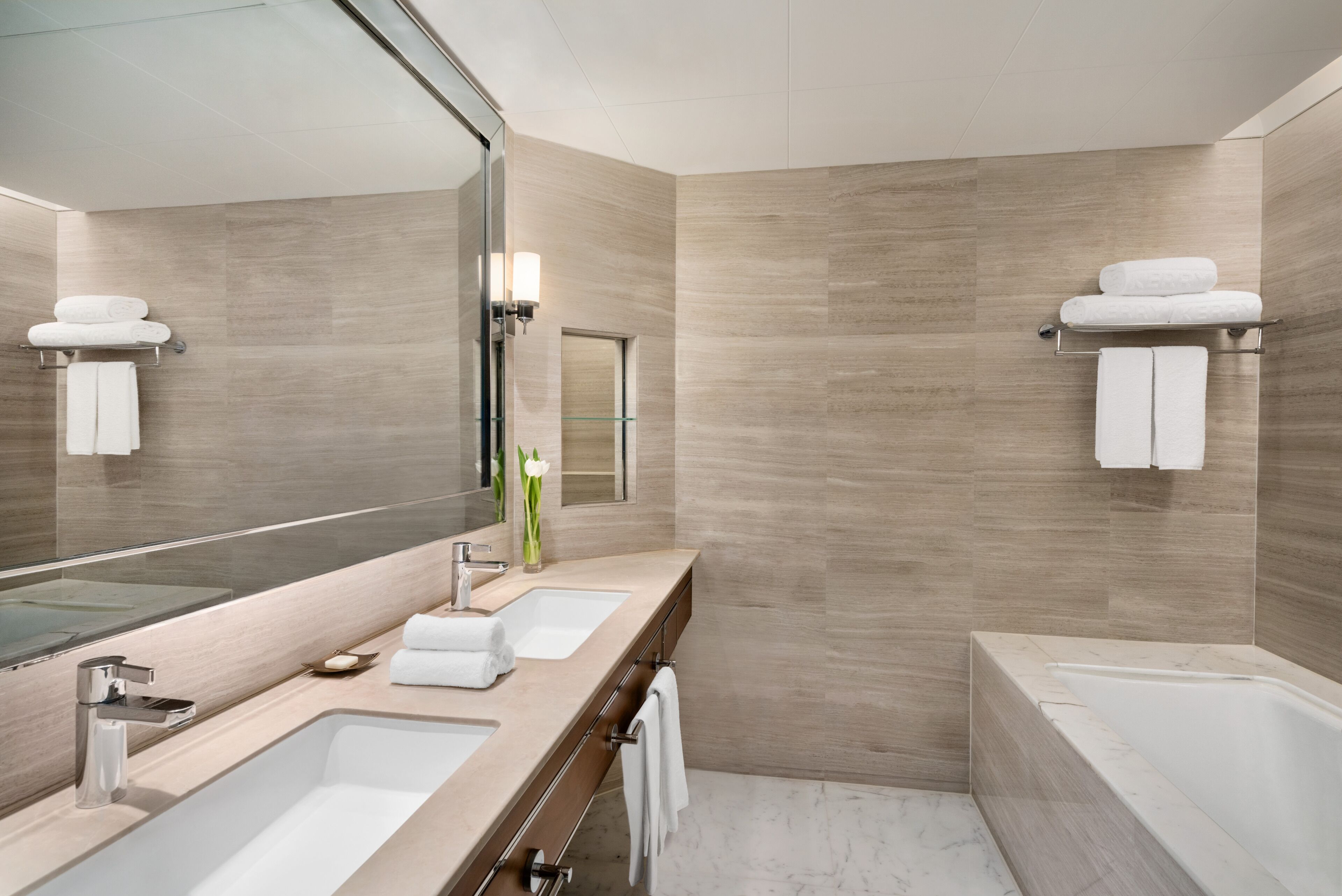 A modern bathroom with two sinks, a large mirror, and a bathtub.