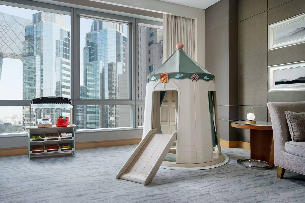 A hotel room with a play area featuring a slide, a small table with a lamp, and a sofa.