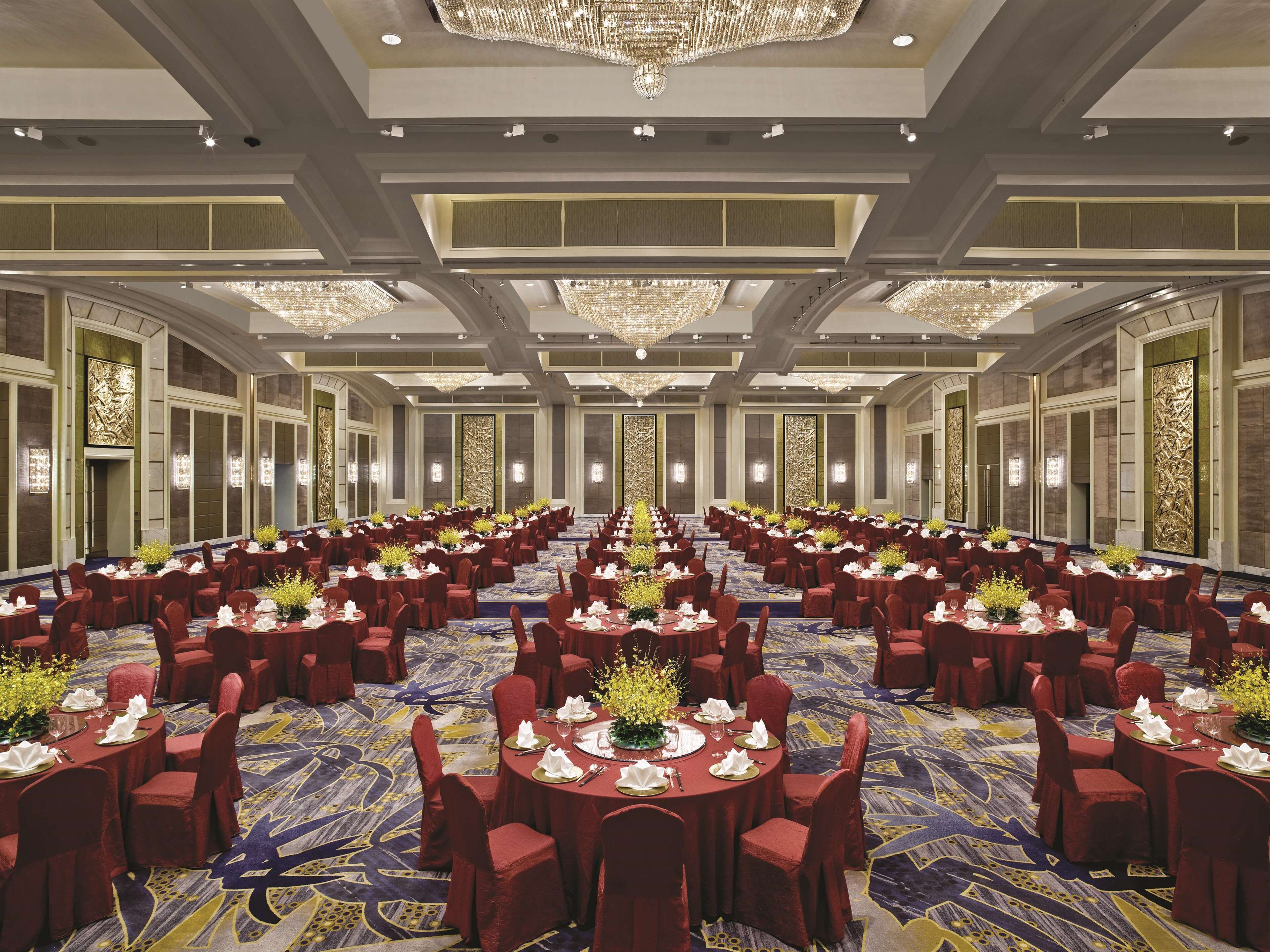 A large banquet hall with round tables, red chairs, and chandeliers.