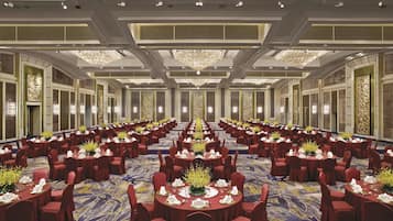 A large banquet hall with round tables, red chairs, and chandeliers.