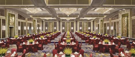 A large banquet hall with round tables, red chairs, and chandeliers.