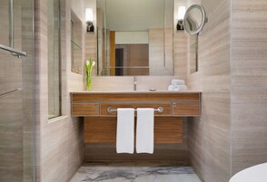 A modern bathroom with a wooden vanity, a glass shower enclosure, and a marble floor.