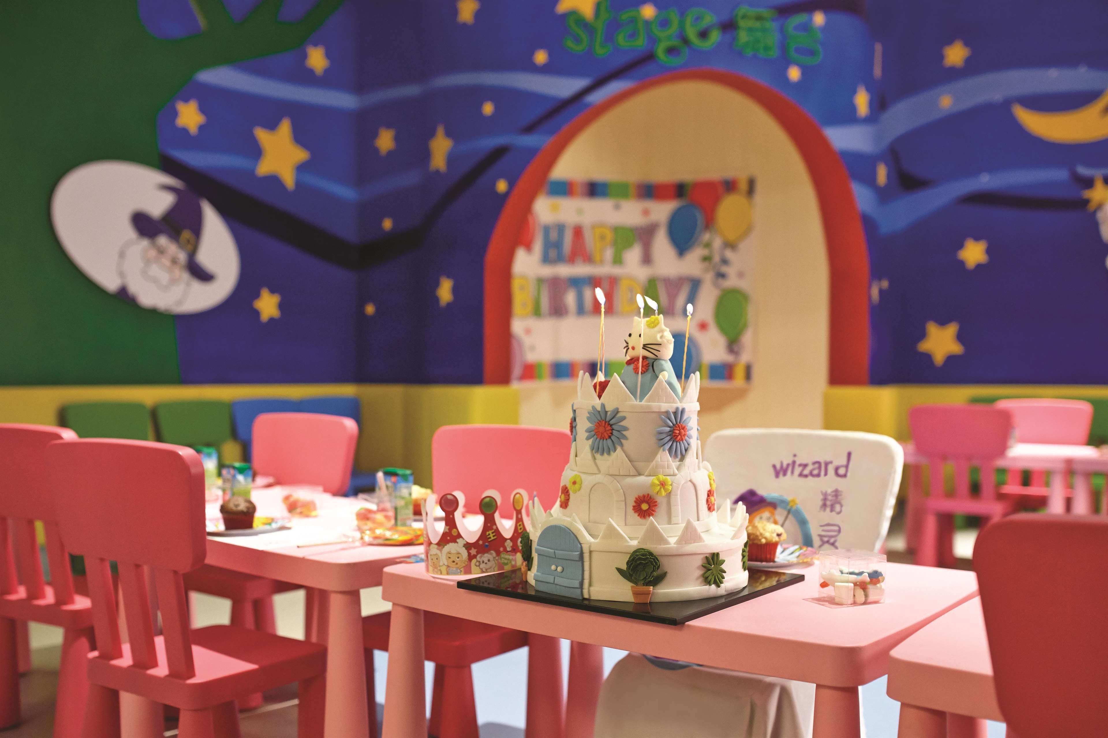 A children's play area with a birthday cake, chairs, and a bookshelf in the background.