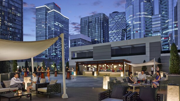 Un espacio al aire libre con mobiliario de mimbre, un bar y vistas a edificios modernos.