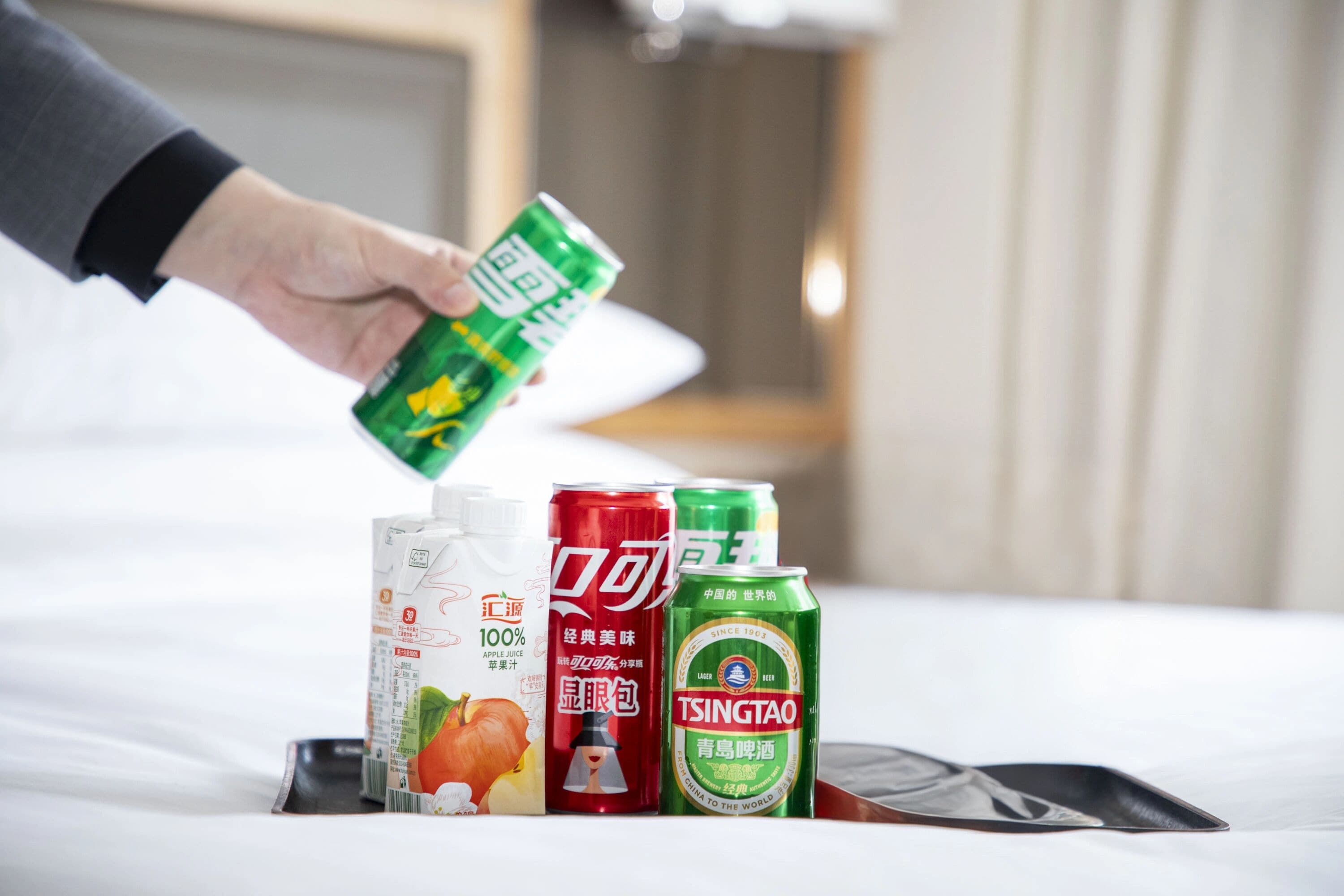 A hand holding a green can, with other beverage cans and a carton on a tray.