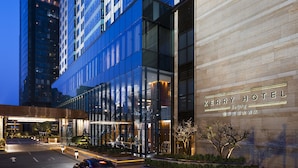 Una entrada de hotel moderna con fachada de vidrio, un letrero que dice "KERRY HOTEL Beijing" y un coche estacionado enfrente.