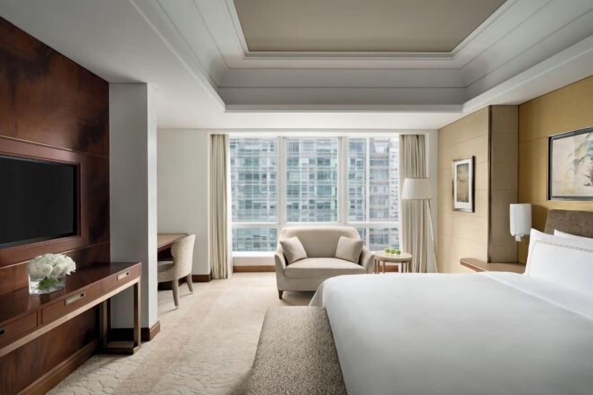 Habitación de hotel con una cama grande, un escritorio, una silla, un televisor y una ventana con vista a la ciudad.