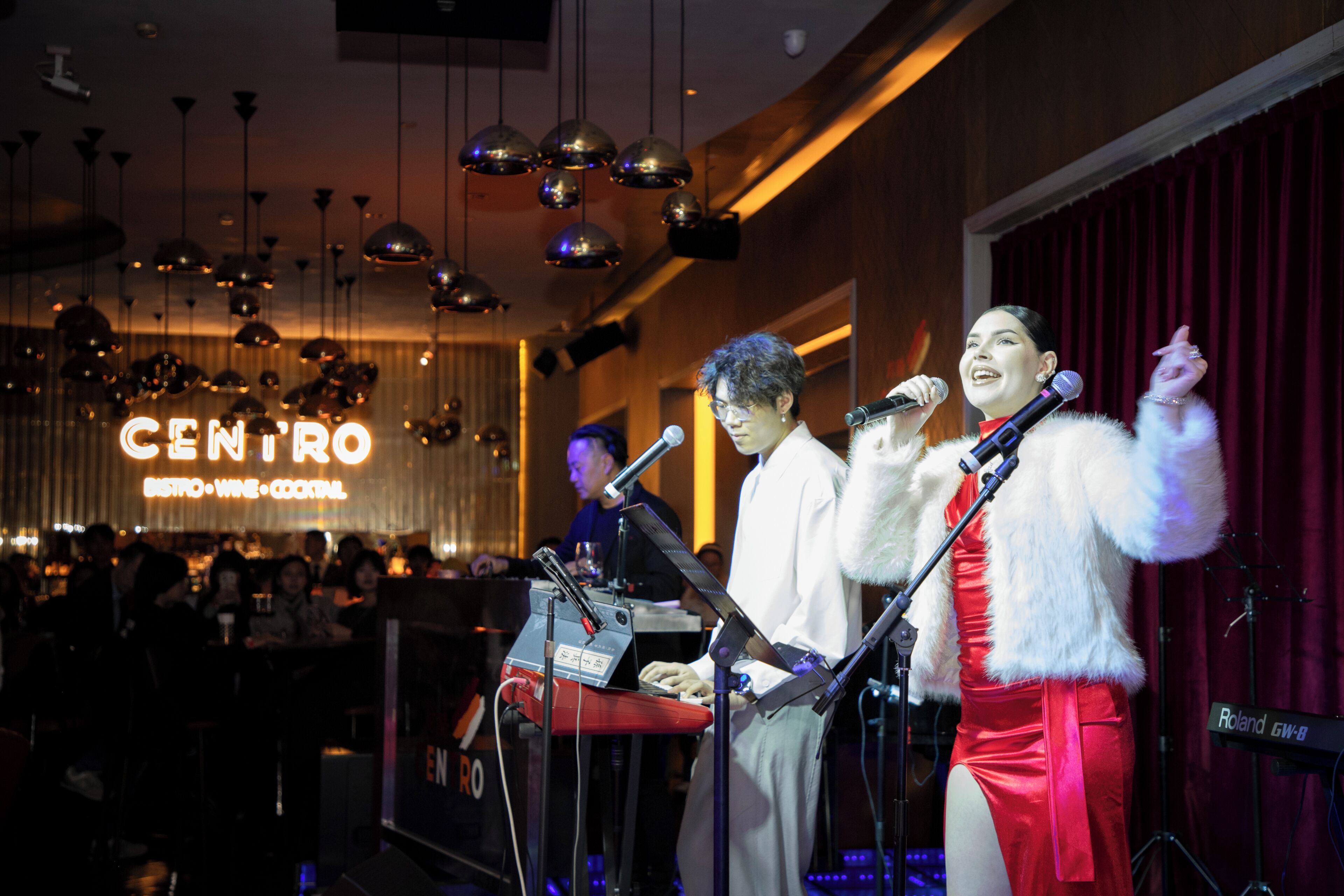 A stage with musical instruments and microphones, a sign reading 'CENTRO BISTRO VINE COCKTAIL', and a crowd in the background.