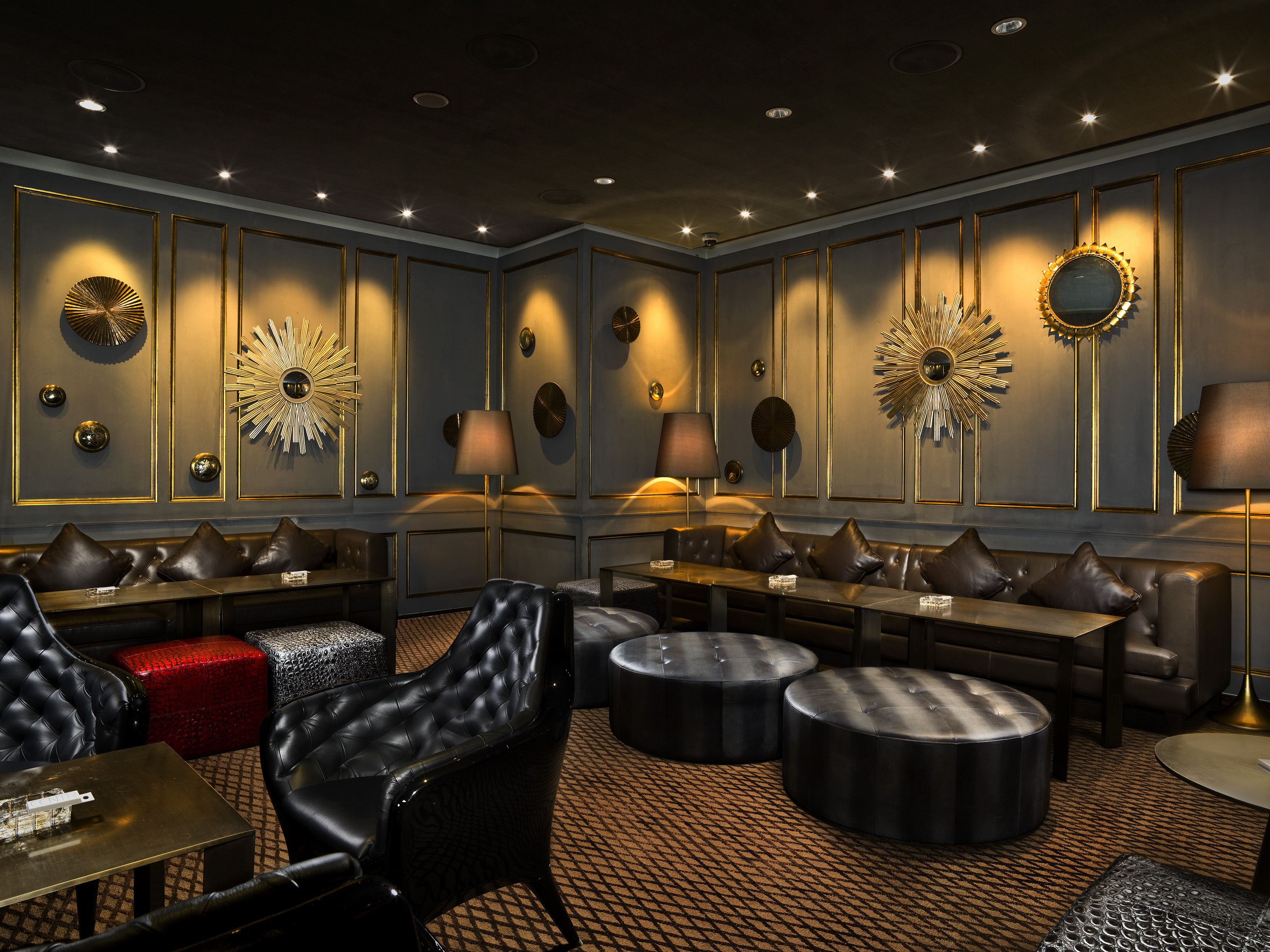 Un espacio lounge lujoso con sofás de cuero, otomanas redondas y decoración de pared elegante.